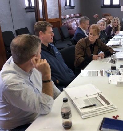 A group of people, including church fundraising consultants, are seated at a table in a meeting room, engaging in discussion and reviewing documents.