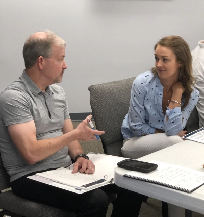 Two people seated at a table are engaged in discussion. Both have documents in front of them.